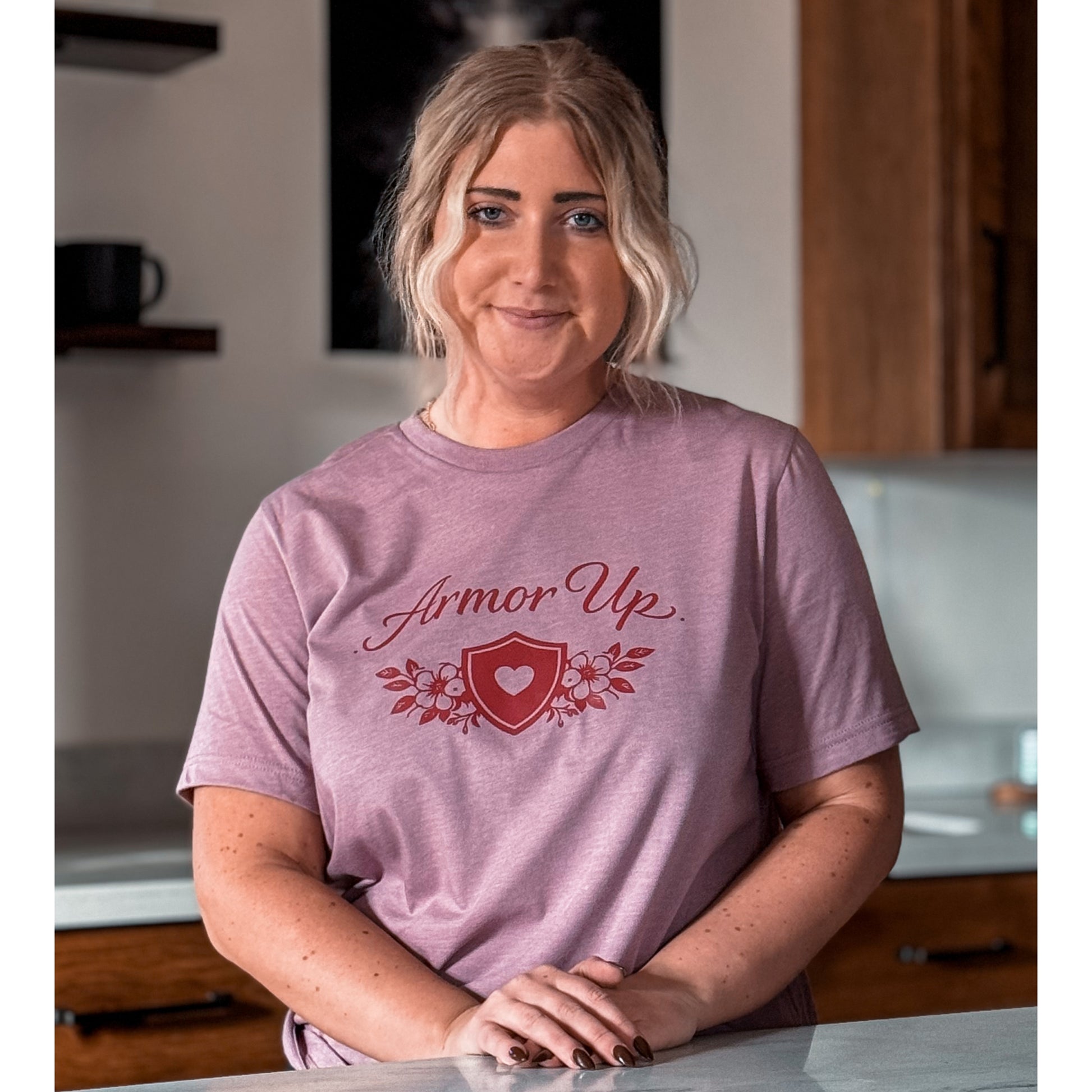 Woman wearing a Pink t-shirt with 'Armor Up' design in a kitchen.