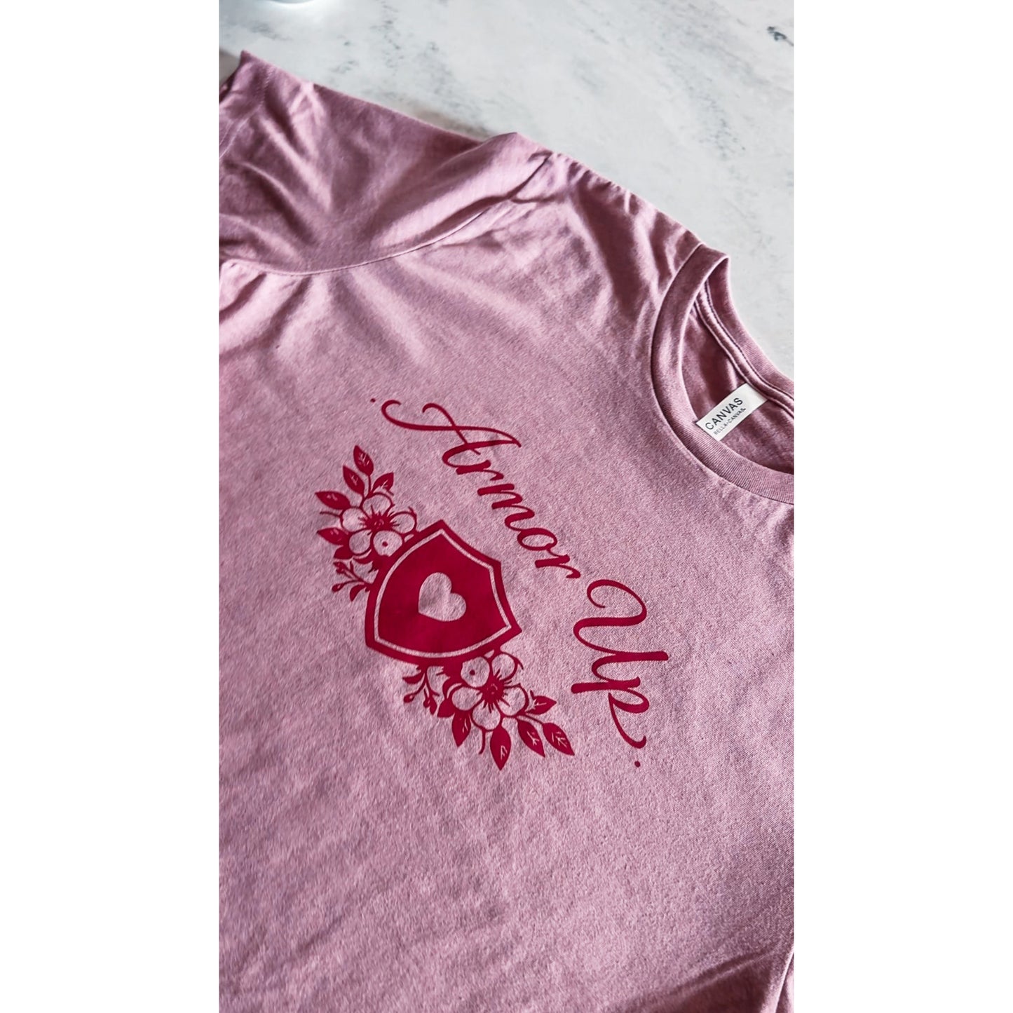 Pink t-shirt with red graphic and text 'Armor Up' on a marble surface
